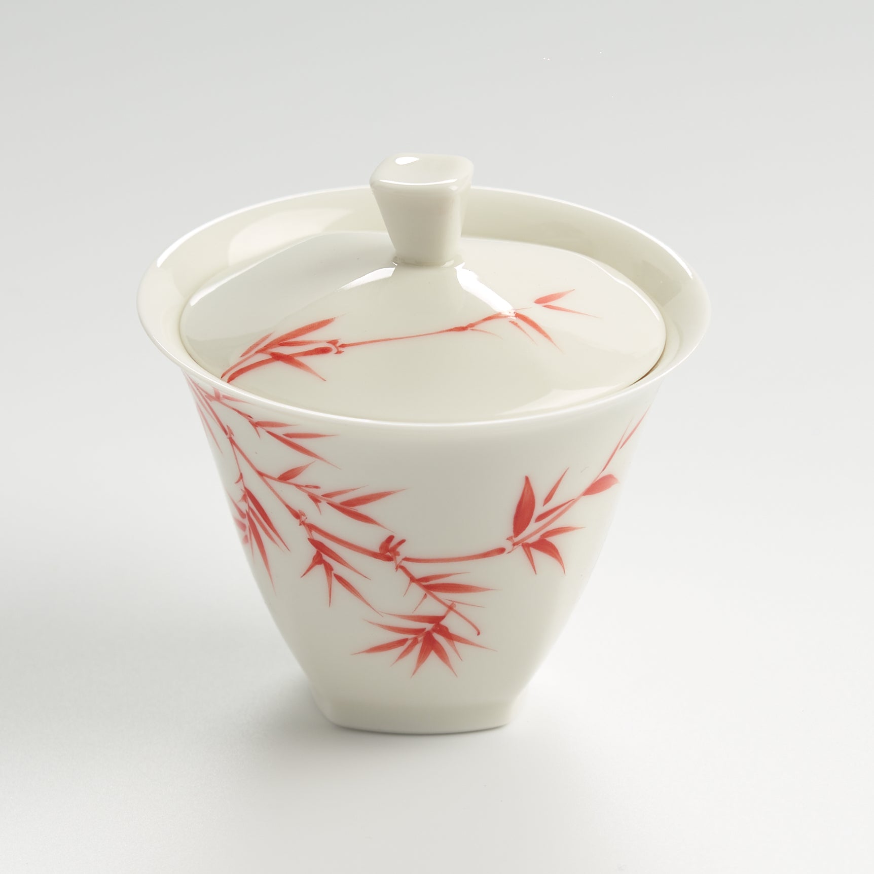 White ceramic teapot with red bamboo design on a light gray background