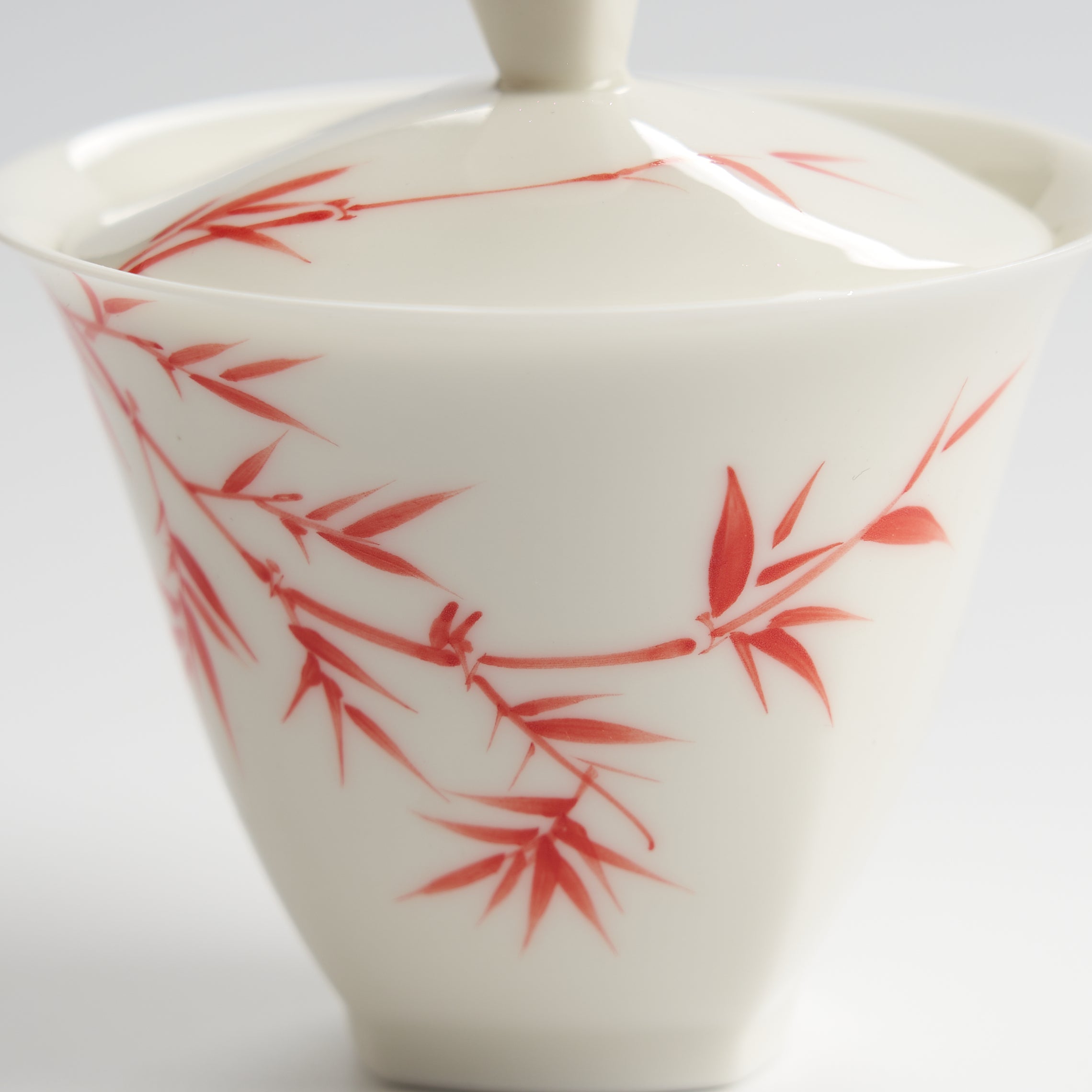 White ceramic teapot with red bamboo leaf design on a white background