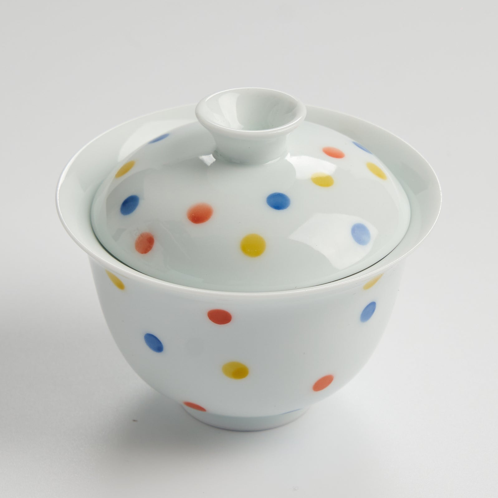 White ceramic teacup with colorful polka dots on a white background