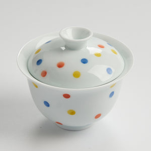White ceramic teacup with colorful polka dots on a white background