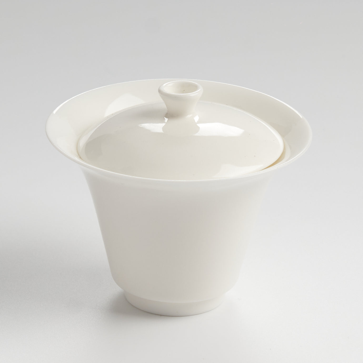 White ceramic teacup with lid on a light gray background