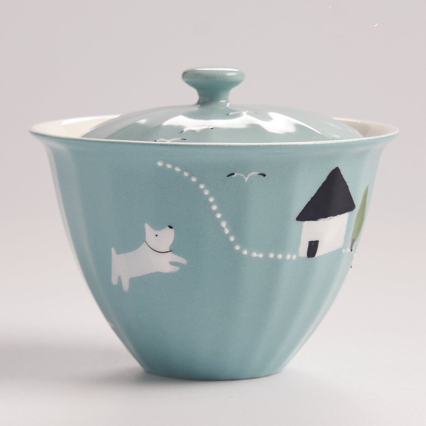 Teal ceramic bowl with a lid featuring a dog and house illustration on a light gray background