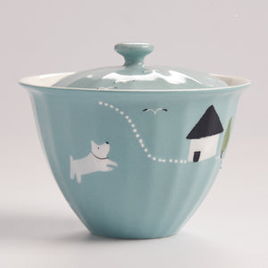 Teal ceramic bowl with a lid featuring a dog and house illustration on a light gray background