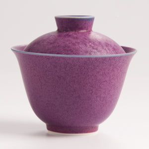Purple ceramic teacup with lid on a white background