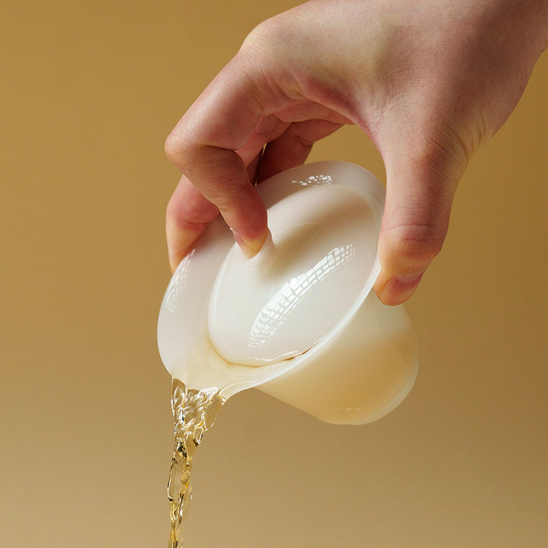 Hand pouring liquid from a jade like gaiwan against a yellow background