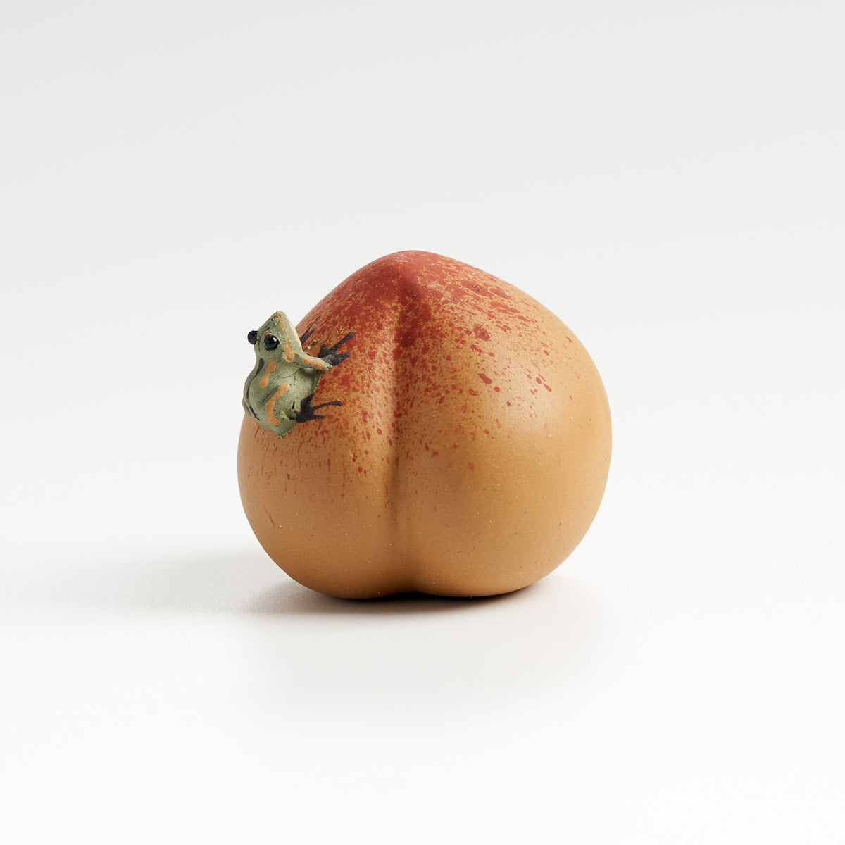 Handmade frog tea pet on a peach, front eye-level view