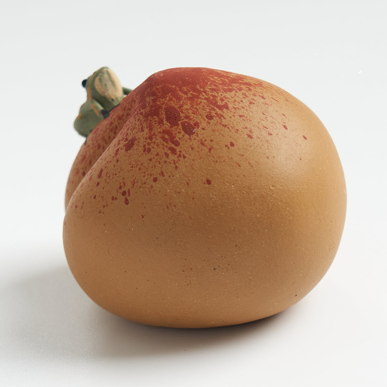 Handmade frog tea pet on a peach, three-quarter rear view