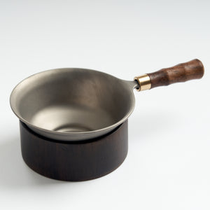 Stainless-steel tea strainer with wooden base, slightly overhead view